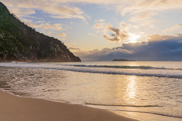 Low angled view of the Sun rising over a cloud bank out to sea past a rocky cliff