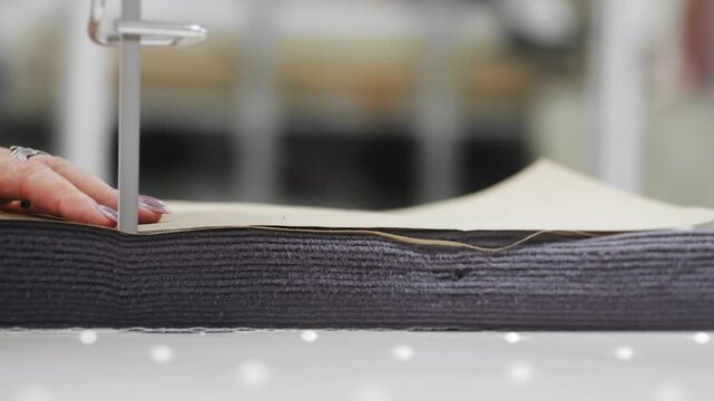 Factory for the production of clothing. A textile factory worker cuts several layers of fabric with an automatic cutting machine.