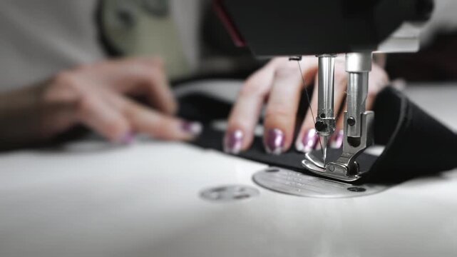 Factory for the production of clothing. Close-up of a sewing machine at work. A girl sews clothes on a sewing machine.