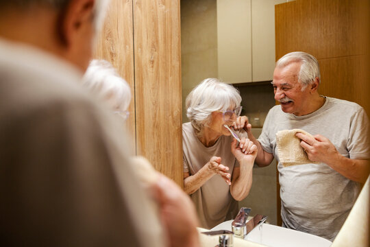 Smiling morning senior couple is having morning routine and brushing teeth in a bathroom.