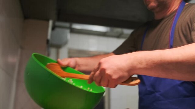 An adult male cook in a blue apron pours devzira rice into a cast iron cauldron to prepare real Uzbek pilaf, slow motion.