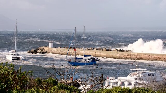 Turbulent ocean waves crash over Hermanus New Harbour pier in stormy weather