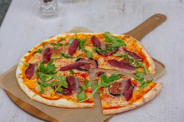 Pizza con hierbas y finas rodajas de carne en una tabla de madera.