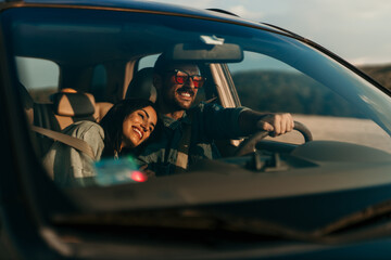 Smiling stylish woman and man sitting in a car and enjoying the ride. Woman leaned on a man's...