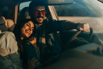 Smiling woman and man sitting in a car and enjoying driving. The woman leaned on a man's shoulder