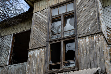 Naklejka premium An old abandoned wooden house with damaged windows and a crumbling roof