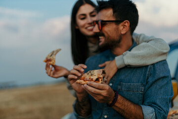 Young Couple Embraced Chatting By Car With Pizza Slice At Hills Watching Sunrise Together