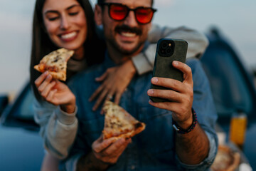 Beautiful young couple enjoying picnic time on the sunset and scrolling the smartphone together