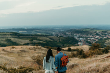 Back view of a young couple standing embraced in tall grass and looking at the view. Man is aiming at a distance. Copy space.