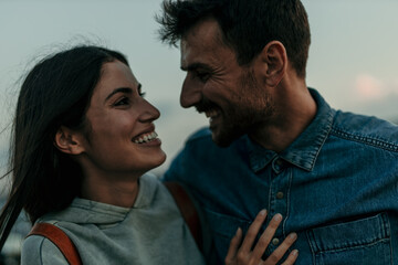 Traveling couple standing outdoors together and laughing during an evening in the hills