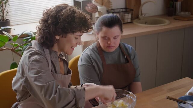 Female culinary teacher explaining how to mix food ingredients in bowl to girl with Down syndrome while giving baking class