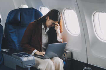 Photo of a frustrated woman sitting on an airplane with her head in her hands. Asian woman sitting...