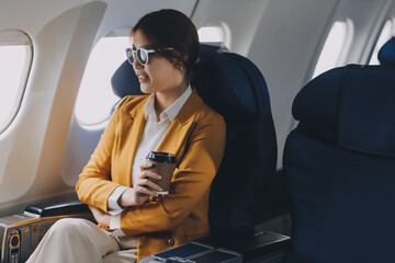 Fototapeta premium A young Asian woman, seated as an airplane passenger, contemplates dollar bills, reflecting on lucrative opportunities and aspirations towards billionaire status.