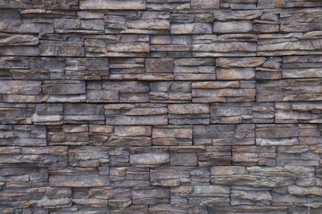 Dark brown stone coating wall made of striped stacked slabs of natural rocks. Panels for exterior. Background and texture.