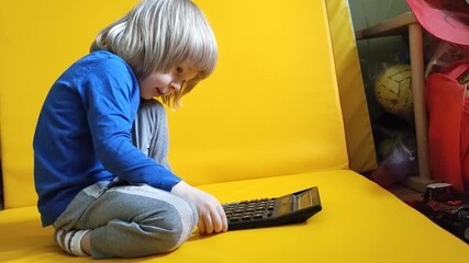 A small child counts on a calculator on a yellow background. Kid fingers press buttons and calculate studying math at home. Child makes arithmetic calculations with a calculator