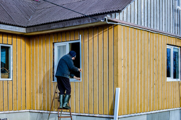 Fototapeta premium Finishing of frame and panel rural house on facade side, roofer installs metal jambs on window opening.