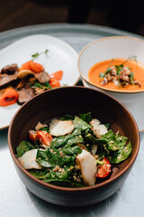 On the table, there is a cream soup with mushrooms, next to it beef with vegetables, and a salad with chicken.