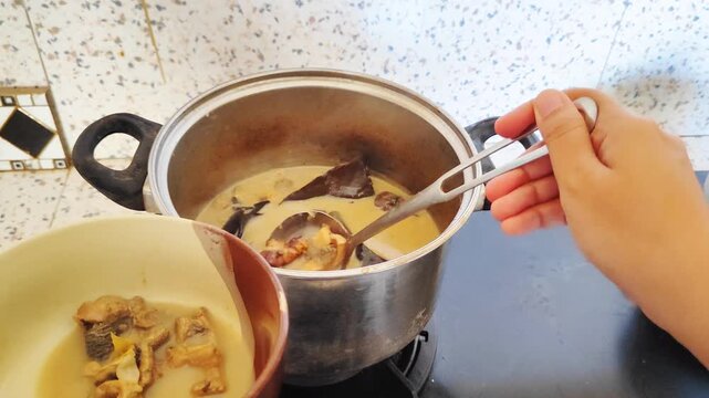 Woman's hand is moving beef curry in a pot to a bowl (Gulai babat sapi)