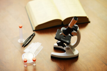 Laboratory Microscope and Open Book on Wood Table with Lab Accessories