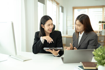 Two smiling business colleagues reviewing marketing reports and discussing project plan at office