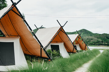 White camping picnic tent  in outdoor park lake with mountains and blue sky with white clouds in the background. Adventure travel and vacation concept