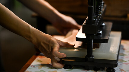Close up shot of leather craftsman working with manual press machine at workbench