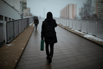 Obraz premium Guy carries suitcase down street.. Man in black clothes on cloudy day.