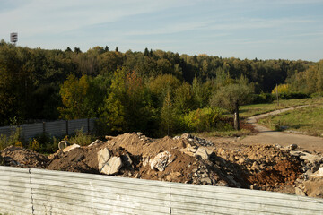 Construction debris behind the fence. Mountain of Earth. Construction details. Abandoned wasteland.