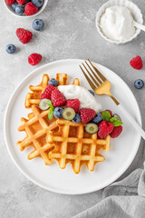 Delicious Belgian Waffle with whipped cream, fresh berries and mint on a white plate on a gray concrete background. Summer breakfast.
