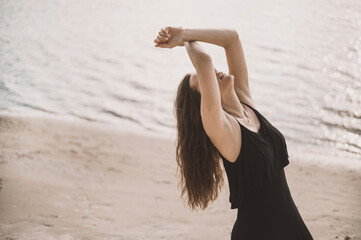Portrait of an attractive woman in a black dress sits on the sand in the desert and the wind...