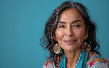 Fototapeta premium A mature Latina woman smiles warmly, showcasing her elegant style with prominent earrings against a vibrant blue backdrop