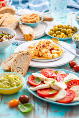 Picnic table with assorted appetizers, raw vegetables, cheese, dips, baguette and pastrami and serrano platter