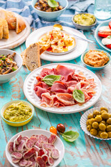 Picnic table with assorted appetizers, raw vegetables, cheese, dips, baguette and pastrami and serrano platter