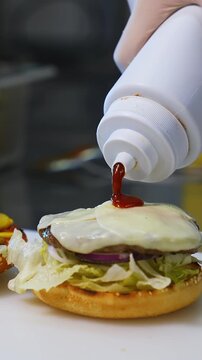 Making hamburger in fast food restaurant. Hand of man smears sauce on a burger and covers with fried bread. Close-up.Tasty burgery ready to eat. Vertical video