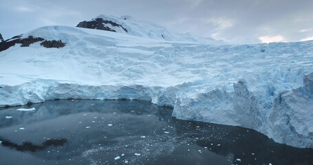 Dramatic massive blue glacier towering in Antarctic polar icy ocean. Snow covered mountains reflection in water. Ecology, melting ice, climate change global warming. Explore Antarctica. Drone flight © mozgova