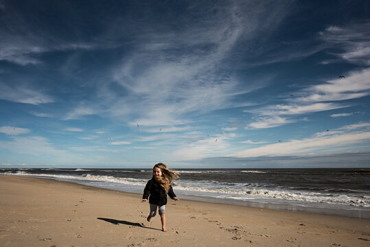 Happy young girl running down beach with seagulls