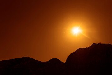 red yellow  Sky with Black Mountain Silhouette. Play of Light. sun set above horizon line. orange golden Sunset above horizon line with sun setting down mountains and sun rays. mountains peak sun beam