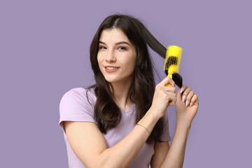 Beautiful young woman brushing her hair on lilac background