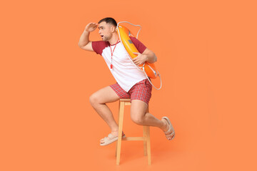 Worried young lifeguard with lifebuoy sitting on stool against orange background