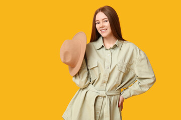 Stylish young girl with hat on yellow background