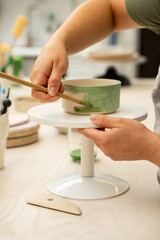 Girl is making a colorful decoration of a clay project with paint and water. Painting ceramic products using acrylic paint and brush.
