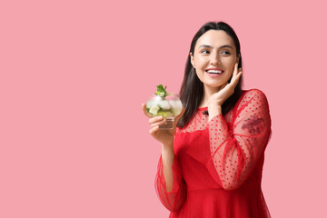 Beautiful young woman with glass of fresh mojito on pink background