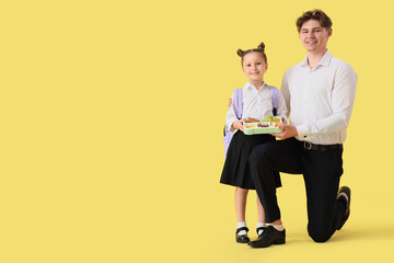 Little girl with school lunchbox and her father on yellow background