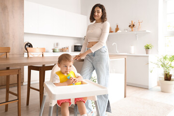 Cute little baby with nibbler and mother in kitchen