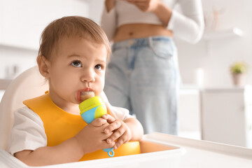 Cute little baby with bib and nibbler eating food in kitchen, closeup