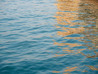 Beautiful close up sea water surface, blue water with golden sunrise reflections. Close-up of golden water with calm ripples surface.