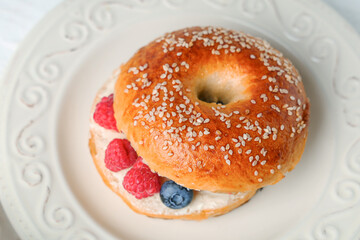 Plate of tasty bagels with butter and berries on white background
