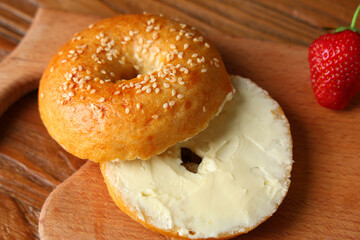 Board of tasty bagel with butter and strawberry on wooden background
