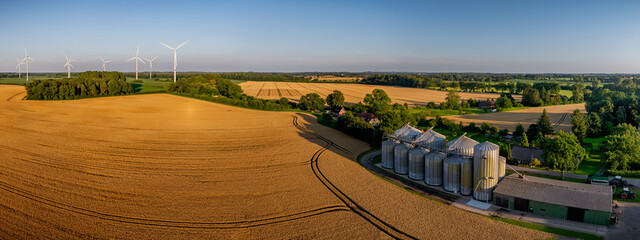 Aerial view of rural landscape with golden wheat fields, silos, farm buildings, barn and wind turbines, highlighting modern agriculture and renewable energy. © snapshotfreddy