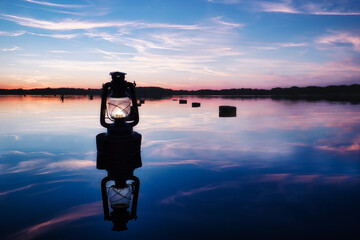 Obraz premium Sunset old Lantern over the Lake - Beautiful - Sky - Background - Lamp - Glow - Seaside - Beach - Kerosene - Lake - Burning - Vintage - Oil - Travel - Wooden - Rusty - Stake - Water - Öllampe